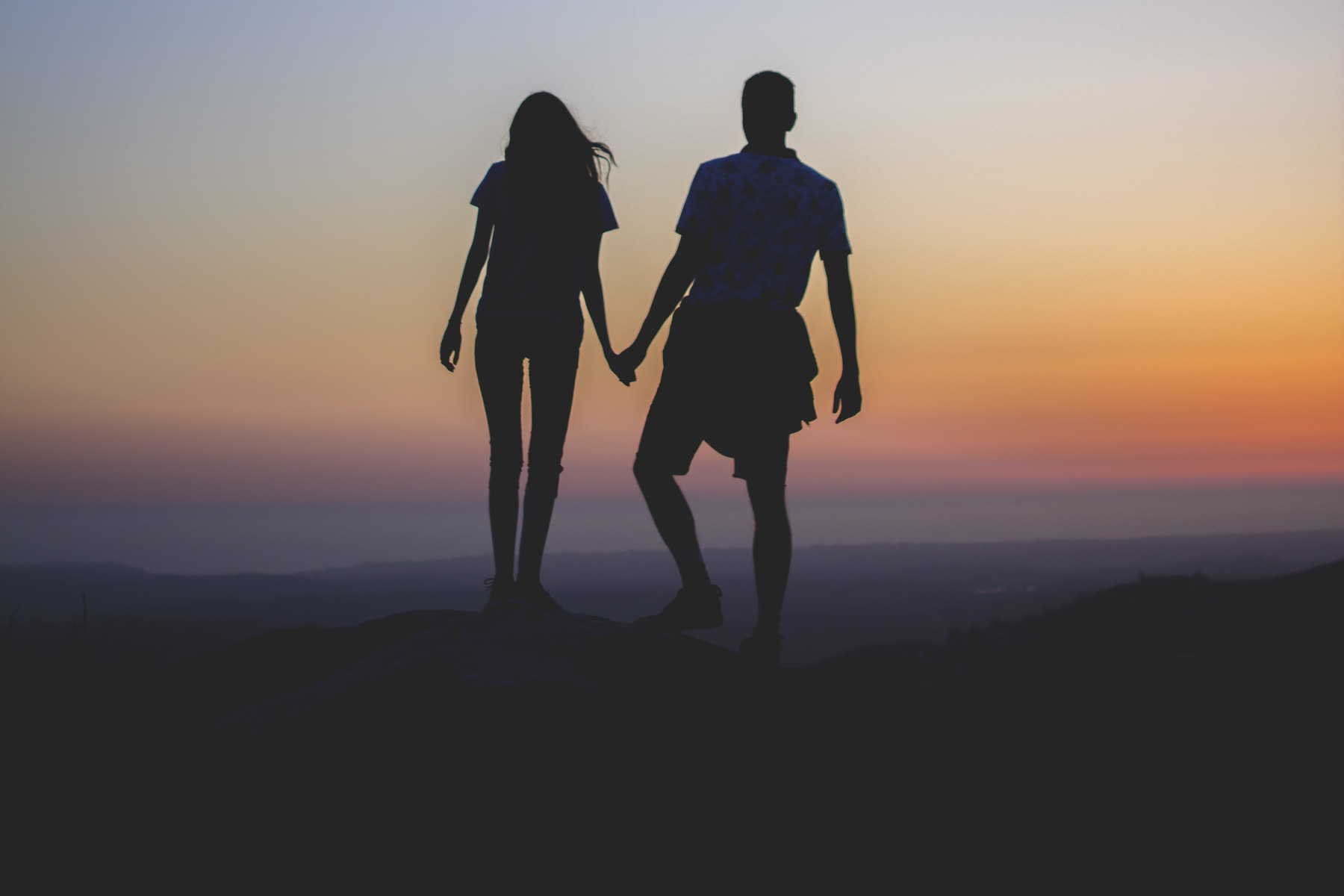 Couple main dans la main, silhouetté face au coucher de soleil